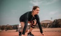 a woman crouches down to pick up a tennis ball