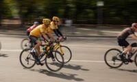 Cyclists in yellow jerseys race on a sunny day.