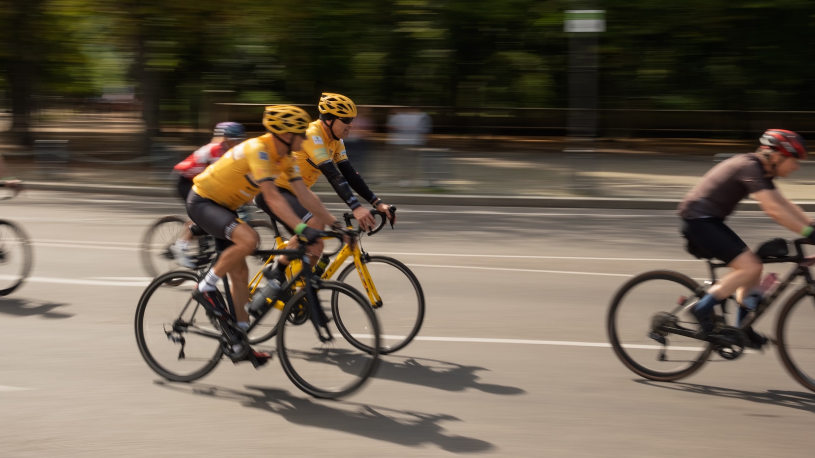 Cyclists in yellow jerseys race on a sunny day.